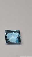 Close-up image of a square princess cut Swiss blue topaz gemstone with lagoon blue color on a plain background.