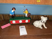 Photo showing the mechanical golf coin bank alongside the cast iron dog figurine on a wooden surface with tags and labels visible.