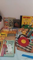 Wide view of assorted children's books and records laid out, showing colorful covers and a stack of 45 RPM records.