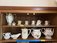 Full view of porcelain set including chocolate pot, cups with saucers, pitchers, and gravy boat on shelves.