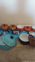 Full view of the cookware set showing multiple pieces in orange and turquoise enamel with lids and black handles.