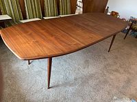 Full view of extended walnut surfboard table with both leaves in place and four tapered legs visible