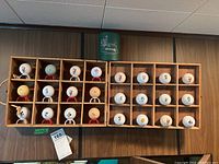 Display of 24 golf balls featuring Disney characters and PGA logos in wooden crate on wall mount.
