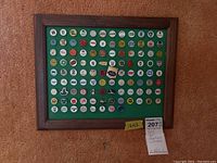 Framed display case with 104 golf ball markers mounted on a green background against a carpeted wall.