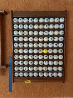 Front view of wooden rack filled with 100 golf balls featuring golf course logos.