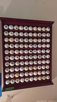 Full view of wooden rack with 100 golf balls arranged in rows, logos visible on several balls.