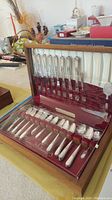 Wooden presentation box containing 58-piece Holmes and Edwards sterling silver plated flatware set displayed upright and flat.