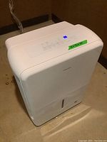 Full front and top view of white Insignia dehumidifier with digital control panel lit, placed on concrete floor.