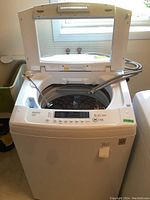 Front view of LG WT1101CW top load washing machine with lid open showing control panel and drum interior.