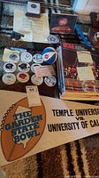 Photo showing NFL Gatorade caps with team logos, NCAA basketball magazines, and Temple University vs University of California Garden State Bowl pennant.