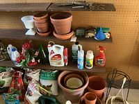 Long view of shelf with various fertilizers, chemicals, small plant pots, and a weather station on pegboard background