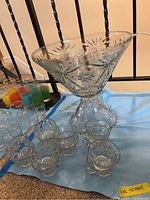 Overall view of punch bowl with pedestal, twelve clear glass cups, and plastic ladle on blue cloth