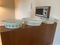 Three vintage Pyrex casseroles with their matching glass lids displayed in a row showing different decorative patterns.