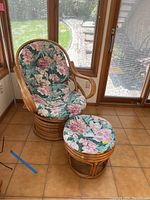 Rattan swivel chair and stool set with floral cushions placed on tiled floor in front of windows showing outdoor steps and lawn.