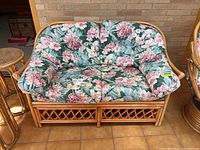 Front view of rattan love seat with floral cushions, showing curved frame and lattice detail.