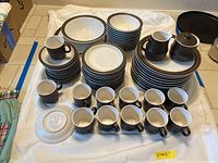 Full set of stoneware dishes including cups, plates, bowls, sugar and creamer set arranged on the floor showing quantity and style