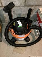 Full view of Ridgid wet dry vacuum with flexible hose coiled and attached nozzle