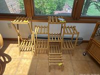 Three wooden slatted stands of varying sizes placed in front of a window on a tiled floor, showing overall set and structure.