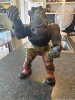 Front view of Rocksteady TMNT action figure showing muscular build, camo pants, helmet, and fists raised.