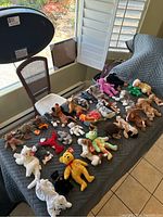Photo showing 32 assorted Beanie Babies laid out on a gray padded surface, displaying varied animal characters and colors
