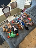 15 assorted Beanie Babies arranged on a bed showing various characters including a frog, panda, moose, and turkey.