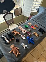 Top view of 17 assorted Beanie Babies arranged on a gray quilted surface, showing different animals and colors.