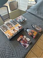 Overview of boxed and blister Star Wars toys on gray blanket including five-pack boxed set, capsule figures, small blister packs, and comic book.