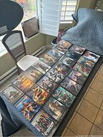 Photo showing 24 DVDs arranged in rows on a cloth-covered surface near a window and chairs, visible DVD covers include action and sci-fi titles.