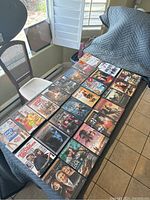 Photo showing 24 assorted used DVD cases arranged on a table, visible movie covers include a variety of genres and actors.