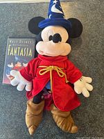 Plush Sorcerer Mickey Mouse wearing red robe and blue wizard hat next to Fantasia VHS tape