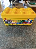 Yellow LEGO Classic large brick storage tub shown from side with LEGO graphics and studs on lid visible
