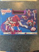 Front cover of Meccano 387 box and purple carry case showing officials logos, model number 387 and images of buildable models including an elephant, robots, and vehicles.