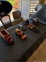 Six toy vehicles arranged on a table including wooden trucks, a construction loader, a Nascar car, and two boxed Revos toys.