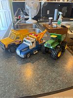 Yellow Tonka dump truck, blue Tonka tow truck, and green John Deere tractor on kitchen countertop