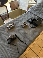 Three vintage cameras and one pair of binoculars arranged on a padded surface, showing general lot contents and condition.