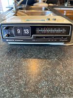 Front view showing the flip clock, tuning dial, volume slider, and power switch on the lower panel.