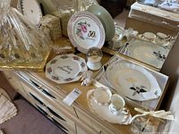 Wide photo showing various 50th anniversary decorative plates, cream and sugar set, snow globe and corsage on a dresser.