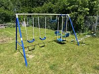 Photo of the backyard swing set with two blue belt swings and two toddler swings on a grassy yard.