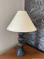 Full view of the carved wooden table lamp showing the stacked, rounded carved sections and cream fabric shade.