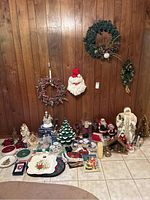 Full view of lot showing large Santa figures, nativity scene, ceramic lighted tree, wreaths, plates, candles, candle holders, table linens, and various serving plates.