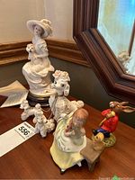 Overall view of collectible figurines including Florence by Giuseppe Armani, Japanese poodles grouping, girl on bench with puppy, and Royal Doulton Bunnykins