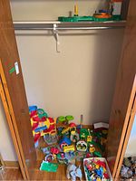 View of farm set pieces arranged on a floor inside closet space showing multiple colorful plastic toy farm components including animals and buildings.