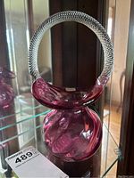 Front view of cranberry glass basket with clear textured handle, showing its shape and color.