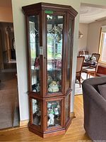 Full front view showing overall shape, glass doors with stained glass design, glass shelves inside, and wooden base.