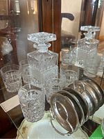 Photo showing the glass decanter with stopper and six matching cut glass glasses arranged on a display surface with a mirror behind