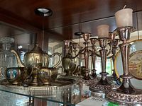 View of the tea set and trio of candlesticks and candelabra arranged on shelf.