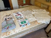 Photo shows all items laid out on a bed including two sweatshirts, several t-shirts, sleeveless and short sleeved undershirts in white with various prints and designs.