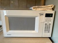 Front view of white GoldStar microwave oven with windowed door and folded table cloth on top.