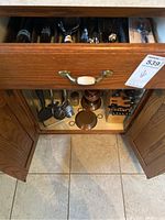 Kitchen drawer partially open showing assorted flatware and utensils organized in compartments and a cutting utensil block with knives inside a cabinet below.