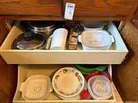Bottom drawer containing assorted plastic storage containers with lids, assorted plates with floral design and plain white, and a clear glass bowl.